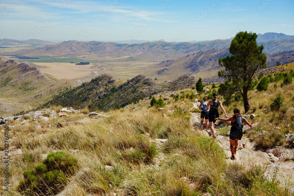 Obraz premium group of three Female Trail Runners running on a stone trail with a scenic arid mountain view