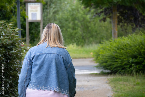 Blonde woman walking through green park wearing denim jacket