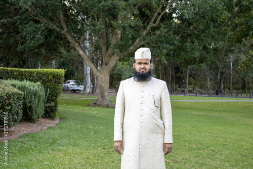 Full-length portrait in traditional formal clothing captured in a spacious green park with tall trees and landscaped surroundings. Natural lighting and open outdoor scenery.