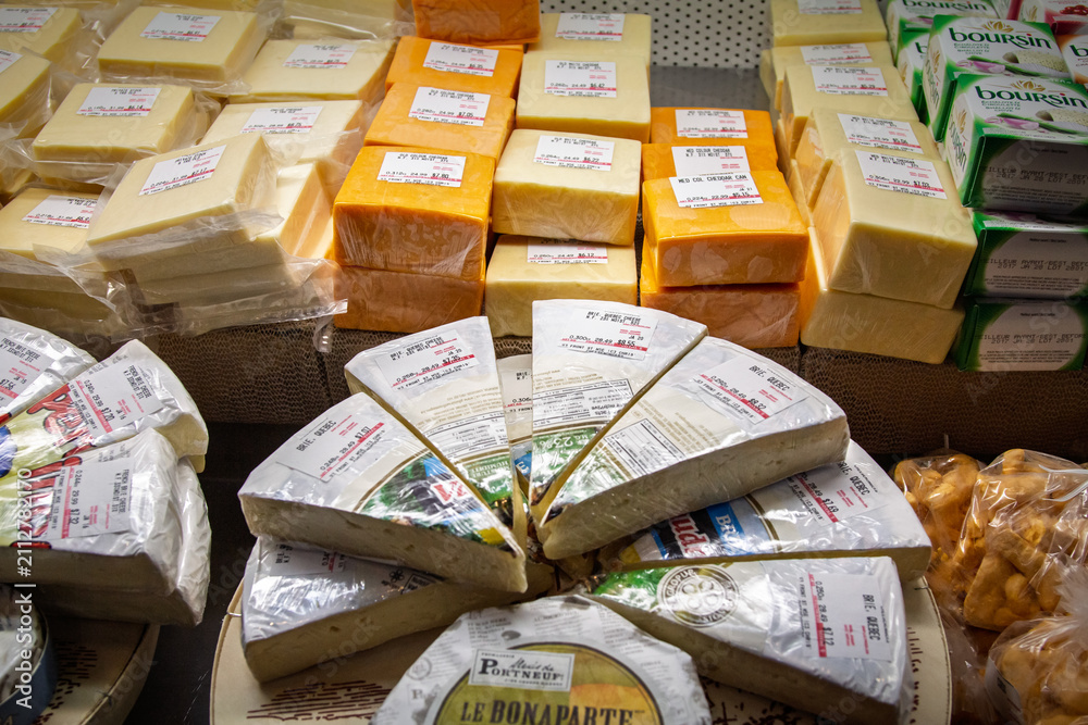 Obraz premium TORONTO, CANADA - DECEMBER 21, 2016: Canadian brie and other cheeses displayed for sale at a Toronto market, with price labels on blocks and wedges of dairy products on grocery costs, food inflation.