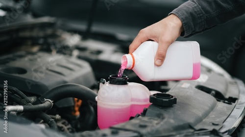 Person pouring pink coolant antifreeze into a car engine coolant reservoir for vehicle maintenance and repair