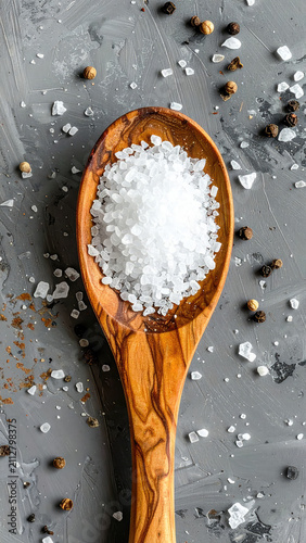 Sea Salt in Wooden Spoon on Gray Surface with Peppercorns