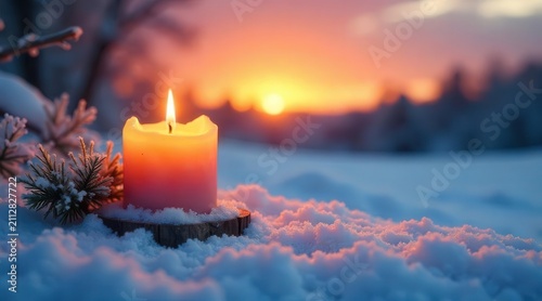 A single illuminated candle rests on a snowy surface at sunset, surrounded by winter branches, creating a serene winter scene.