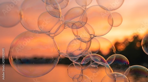 Colorful soap bubbles floating at sunset with warm orange and pink sky reflecting light and nature in their thin translucent surfaces