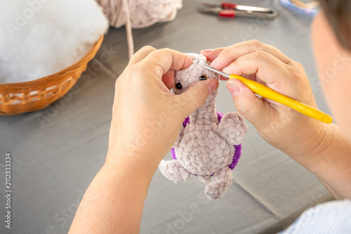 Hands of craftswoman stitching soft plush turtle head using crochet hook. Detailed view of creating handmade amigurumi toy during craft masterclass tutorial