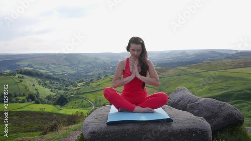 Yoga practice on a mountain top in nature with a clear sky and green valleys in the background