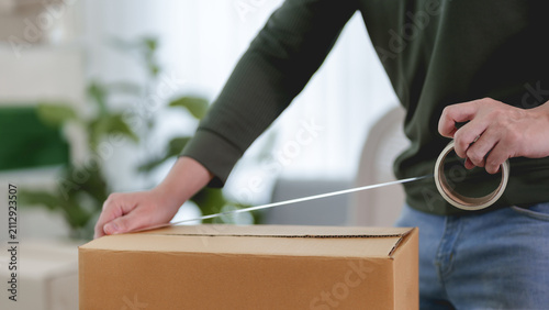 Woman sealing cardboard shipping box with packing tape in bright home workspace for ecommerce business