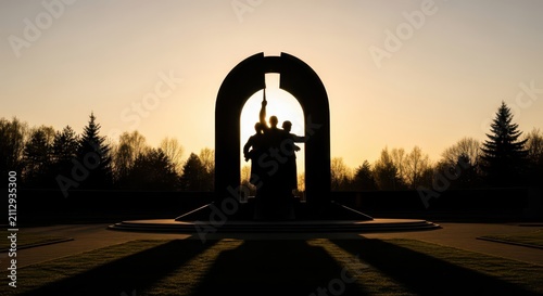 Silhouette of a monument with figures against a sunset sky, trees in the background, park setting