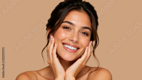 Close up portrait of smiling young woman touching her face. Natural beauty and healthy glowing skin concept on beige background