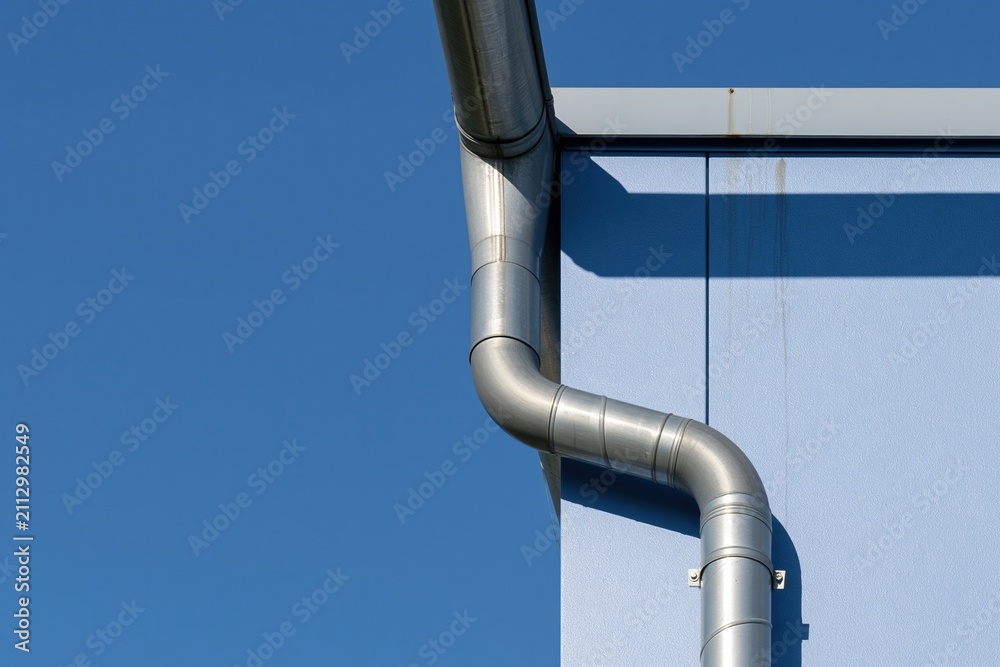 Naklejka premium Modern metal downspout and gutter system on a blue building facade showing architectural details for roof drainage and home exterior maintenance