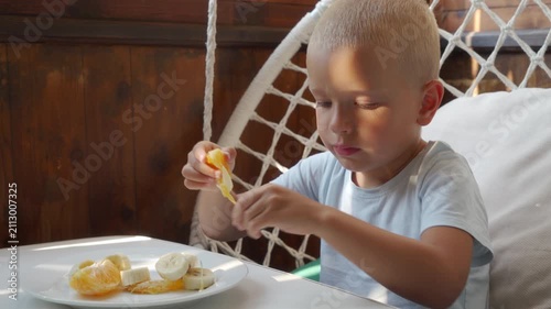 Close view of young boy concentrating as he peels tangerine and eats snack at table in cozy indoor room with soft natural light, capturing calm childhood lifestyle moment, with boy, child, tangerine