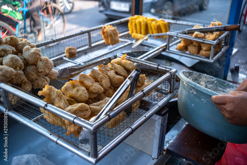 Canvas Print Assorted deep-fried snacks displayed in wire mesh racks on a street food cart, showcasing a selection of popular Indonesian street food