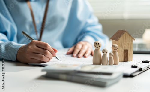 Konstfotografi Business professional completing home insurance documents with family and house models, representing property protection, financial planning, homeownership, risk management, and insurance coverage
