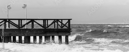 Konstfotografi Black and white image of a wooden pier or boardwalk with rough sea waves crashin