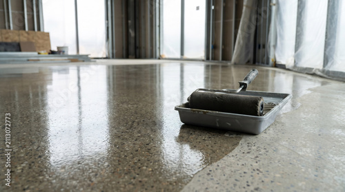 Freshly sealed polished concrete floor with wet roller sheen and paint tray at the edge