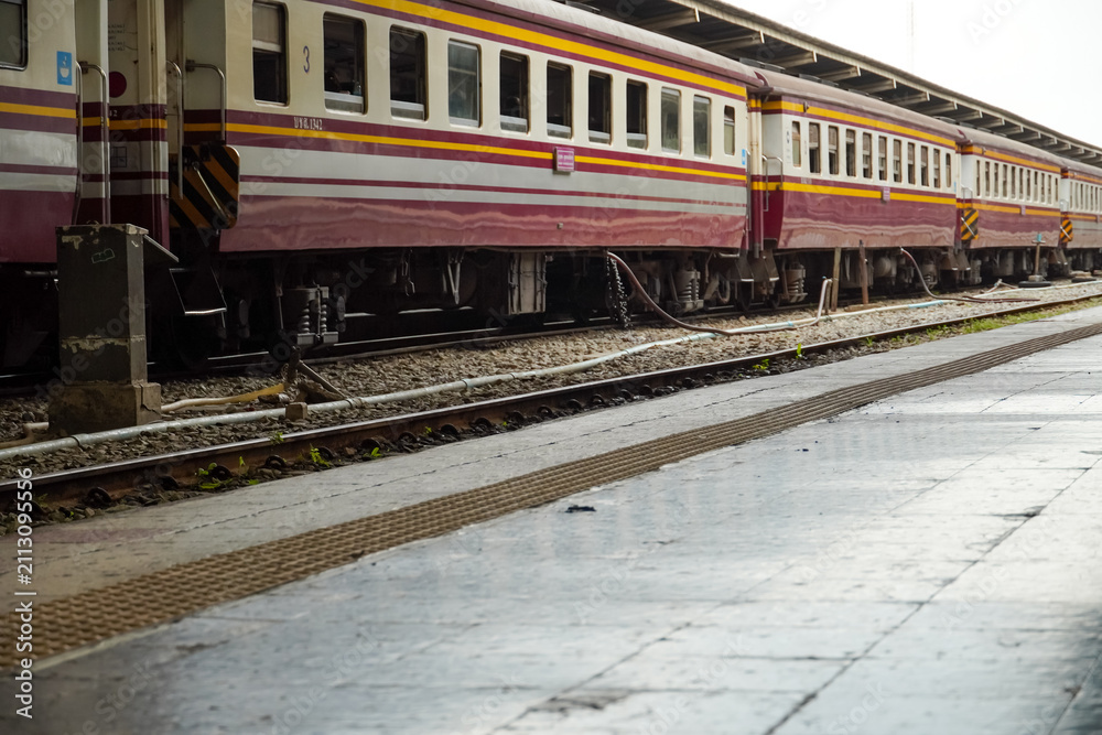Fototapeta premium Passenger train with maroon and yellow stripes parked at a station platform