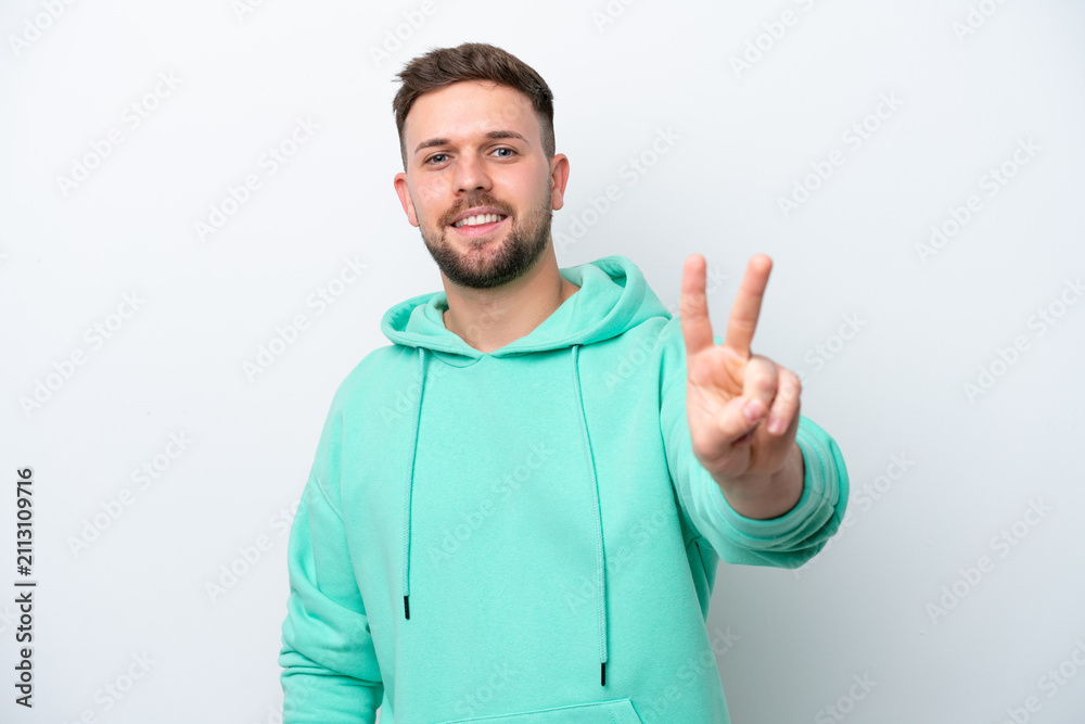 Fototapeta premium Young caucasian man isolated on white background smiling and showing victory sign