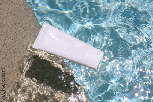 Blank white cosmetic tube mockup floating in sparkling pool water