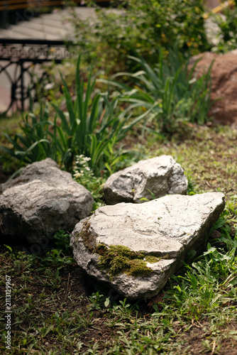 Large natural decorative stones with green moss placed in a park garden landscape.