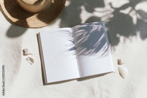 Blank white book mockup in sand with straw hat and seashells