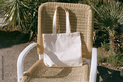 Blank white canvas tote bag mockup on wicker chair with palm plants