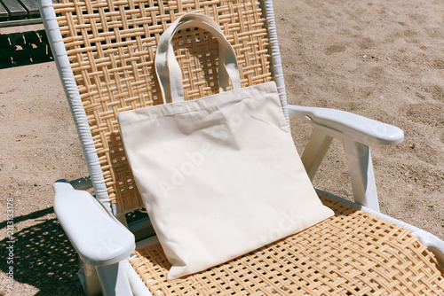 Blank white canvas tote bag mockup on rattan chair in the sand