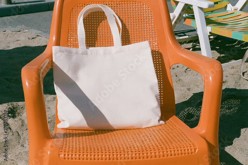 Blank white canvas tote bag mockup on orange chair at the beach