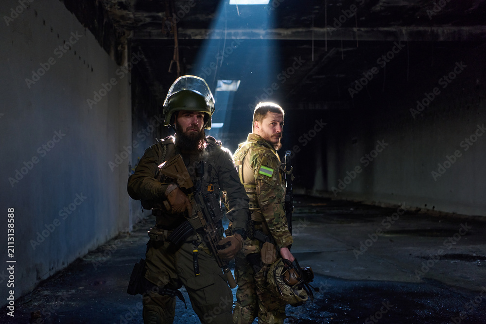 Obraz premium Two Soldiers in Tactical Gear Standing Back-to-Back in Dark Urban Military Interior