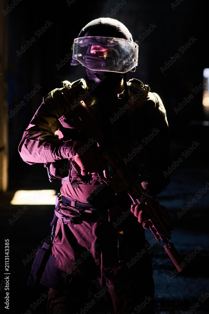 Obraz premium Tactical Soldier in Ballistic Helmet and Visor Holding Rifle in Dark Urban Environment