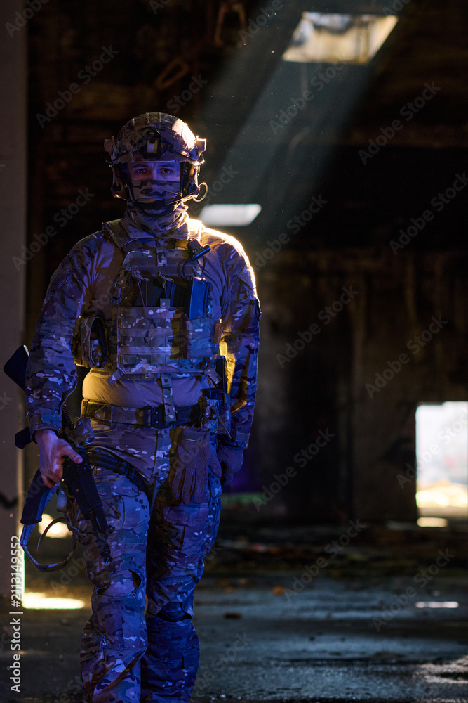 Obraz premium Armed Soldier in Camouflage Tactical Gear Walking Through Dim Urban Ruins With Dramatic Light