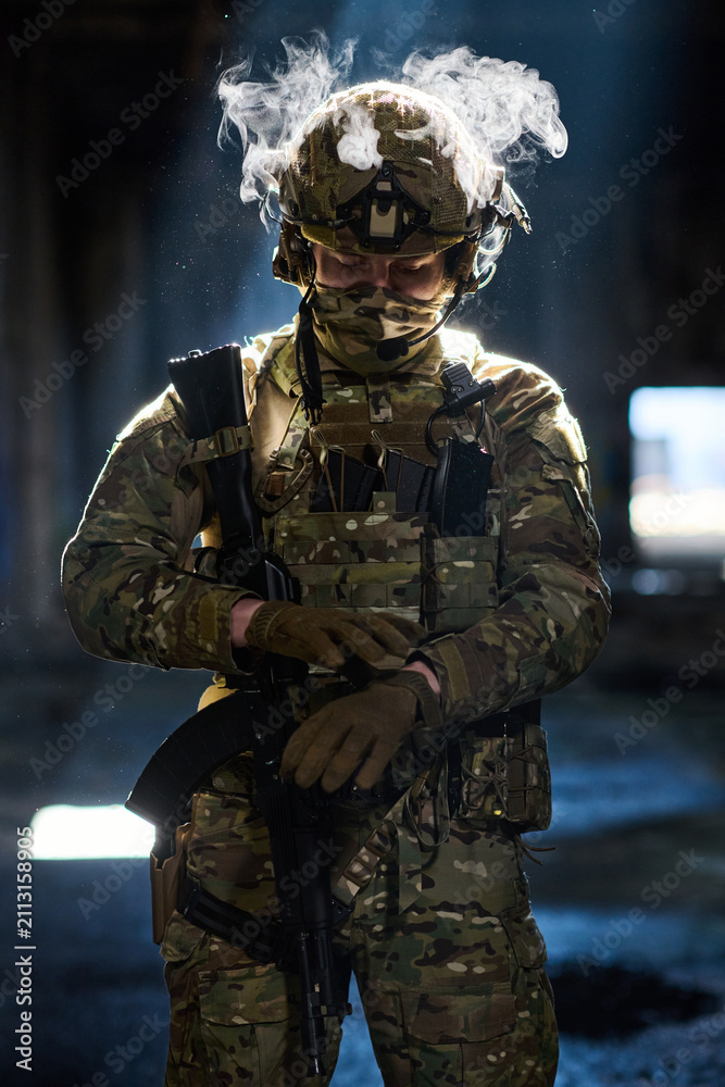 Obraz premium Armed Soldier In Tactical Camouflage Gear With Helmet And Rifle Standing In Dim Urban Environment