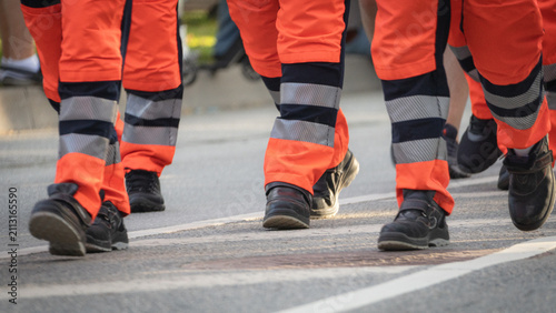 Obraz na plátne Low-angle view of emergency service personnel wearing high-visibility orange protective trousers as they march together during a public city parade