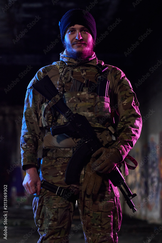 Obraz premium Armed Soldier in Camouflage Tactical Gear Holding Rifle in Urban Night Environment