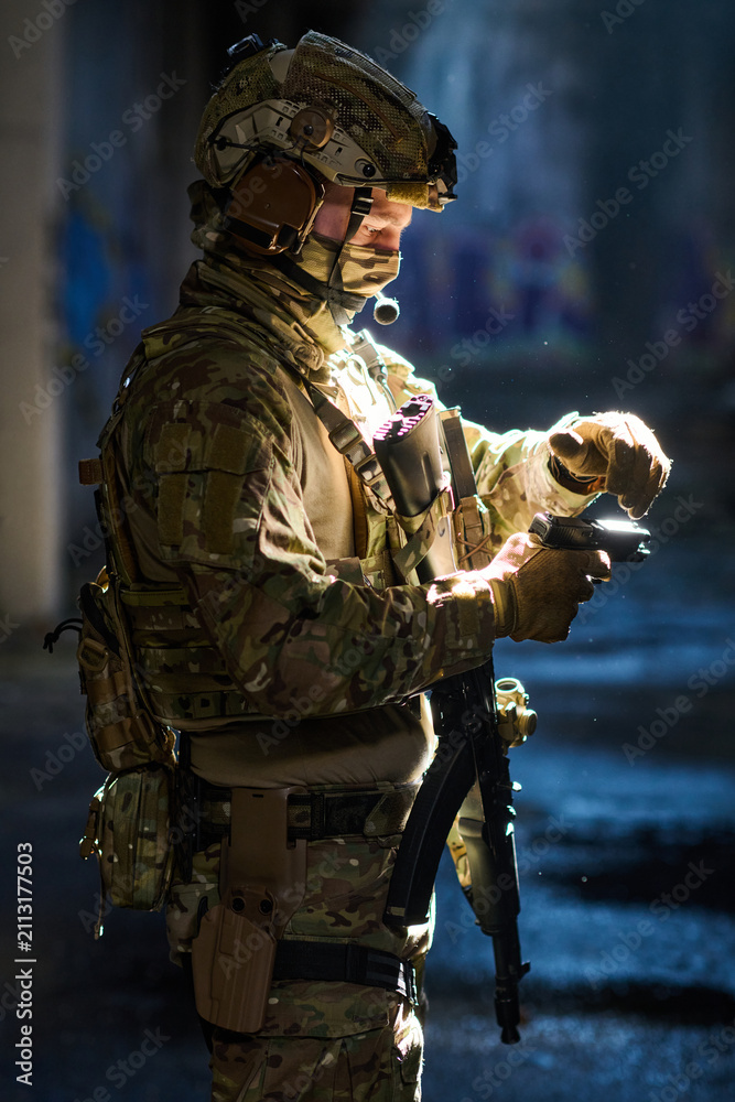 Obraz premium Tactical Soldier In Camouflage Gear Preparing Handgun During Night Operation With Rifle and Helmet