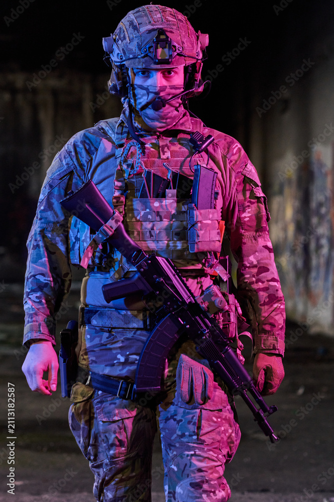 Obraz premium Armed Soldier In Tactical Gear Wearing Helmet And Camouflage With Assault Rifle In Urban Night