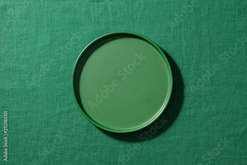 Empty green matte plate on green fabric background. Close up, copy space, top view.