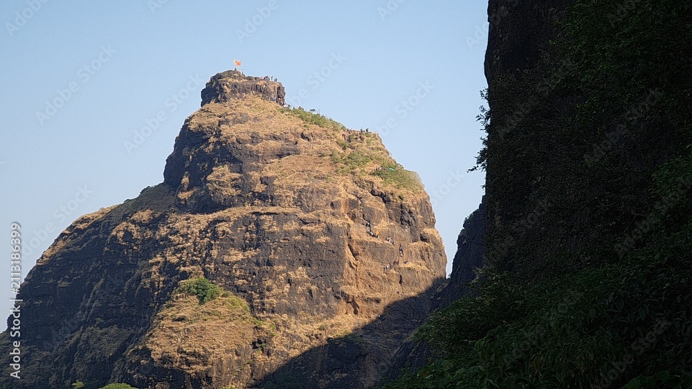 Fototapeta premium Kalavantin Durg pinnacle with trekkers climbing steep steps near Prabalgad Maharashtra India