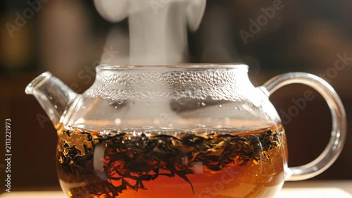 A clear glass teapot filled with freshly brewed hot black tea, releasing a gentle steam in the kitchen