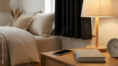 Warm bedroom nightstand scene with smartphone, books, lamp, and alarm clock, showing evening routine, sleep hygiene, and circadian rhythm habits