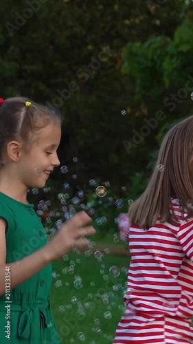 Camera movement on happy children play with soap bubbles in summer park. Kids leisure outdoors. Vertical shot
