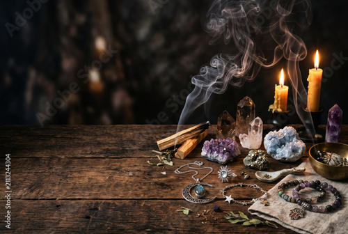 Mystical altar with incense smoke, candles, crystals and celestial jewelry arranged on an aged wooden surface. Spiritual rituals and meditation concept. Copy space