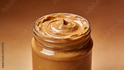 Creamy Peanut Butter in an Open Glass Jar on Brown Background