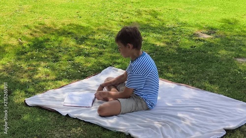 Young Boy Reading Book Sitting on Blanket in Green Park