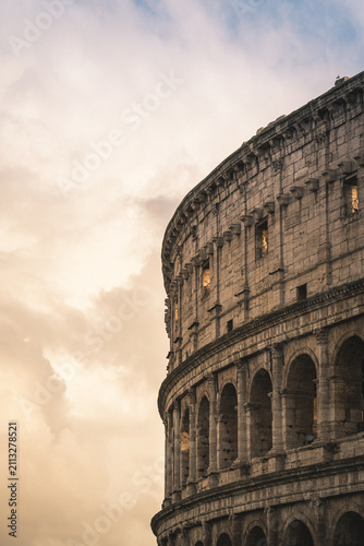 Colosseum, an iconic Roman amphitheater and UNESCO World Heritage Site, stands against a warm, cloudy evening sky, illustrating historic architecture and cultural heritage in Rome