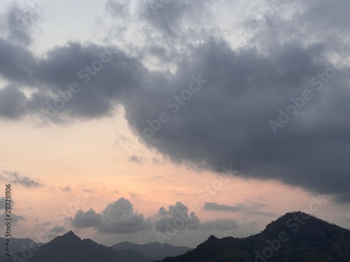 Moody dark clouds over mountain silhouettes at sunset. Dramatic mountain landscape with warm twilight sky for nature backgrounds.