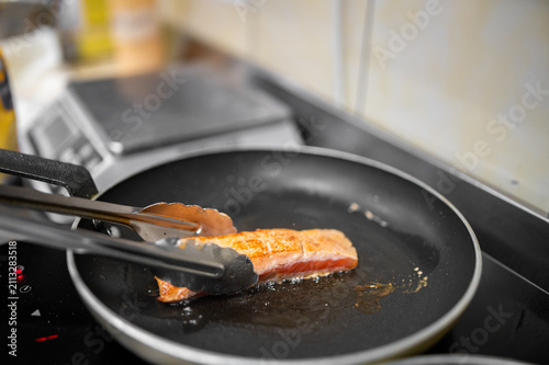 Принти на полотні Salmon fillet searing in a hot non-stick skillet on a kitchen stove, being flipped over with kitchen tongs
