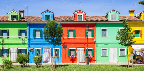 Panorama of symmetrical colorful houses behind young green trees in Burano, Venice, Italy