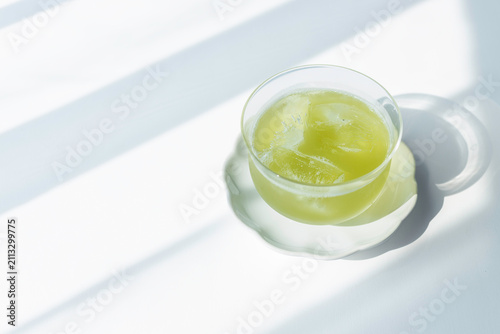 Glass of iced green tea in sunlight on white background with copy space