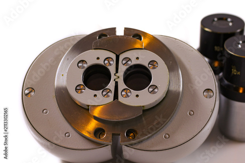 Macro close-up of a stereo microscope objective mount and optical head with precision metal components isolated on a white background.