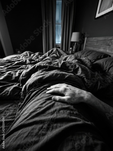 Man's Hand Resting On Unmade Bed Sheets In Dark Bedroom